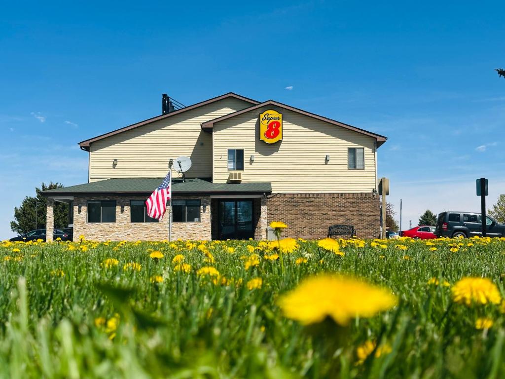 a building with a flag and a field of flowers at Super 8 by Wyndham Imlay City in Imlay City