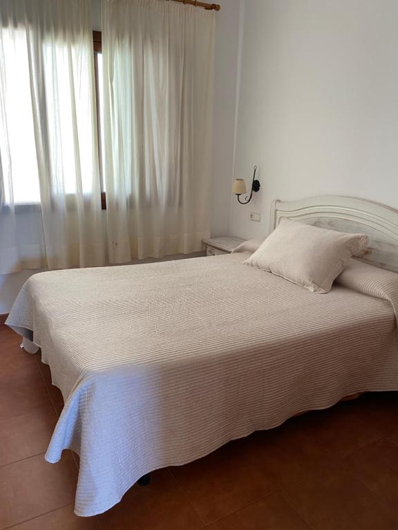a white bedroom with a large bed with white sheets at Apartamentos LLorca in Platja de l’Almadrava