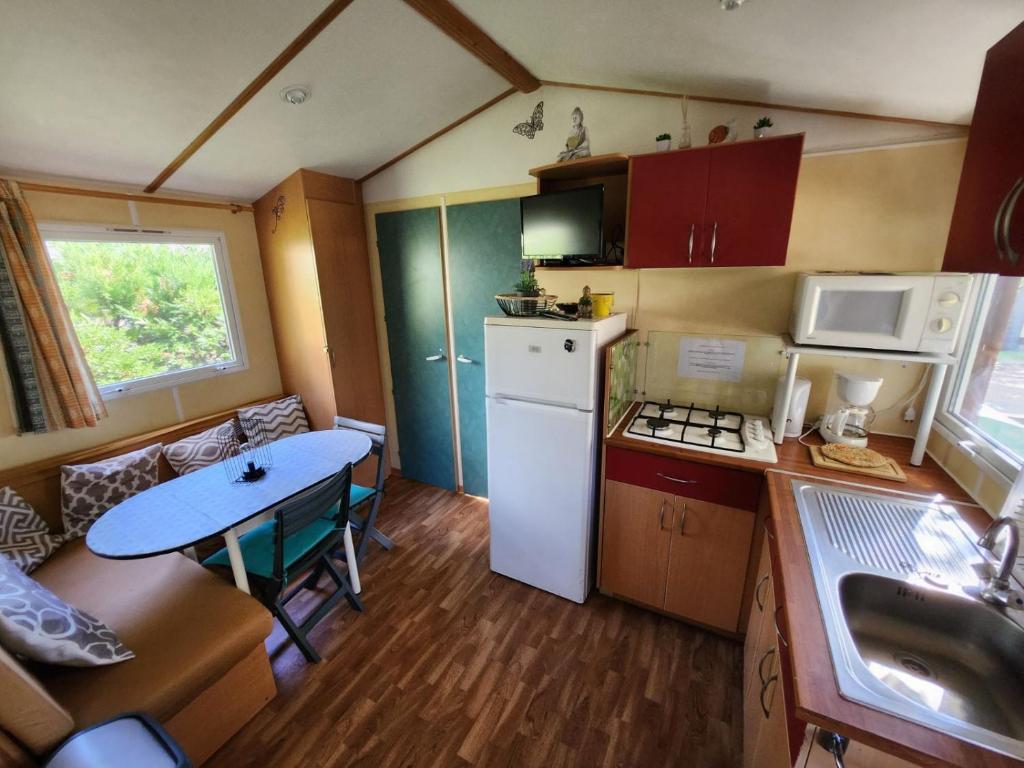 Una pequeña cocina con una mesa y un refrigerador. en MOBIL HOME DANS CAMPING 3 etoiles GORGES DU VERDON CALME 4 PERS PLANCHA, en Sainte-Croix-du-Verdon