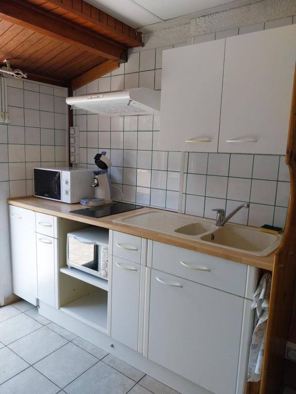 une cuisine avec des armoires blanches, un évier et un micro-ondes dans l'établissement La Maison de la Plage, à Port-la-Nouvelle