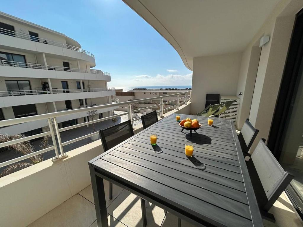 une table en bois sur un balcon avec un bateau de croisière dans l'établissement Panaréa Cieu, à Valras-Plage