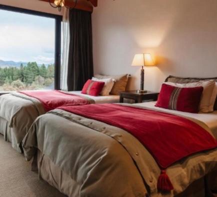 two beds in a hotel room with a large window at El filo del Lolog in San Martín de los Andes