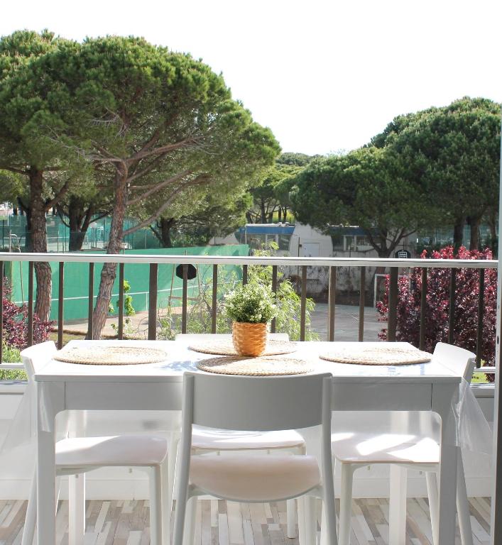 une table et des chaises blanches sur un balcon arboré dans l'établissement Appartement cosy à Port Camargue, au Grau-du-Roi