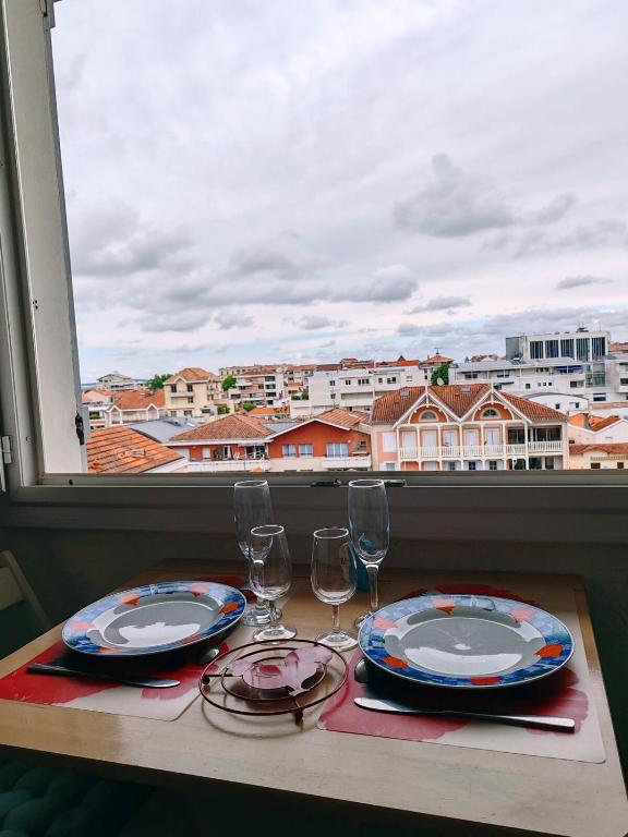 une table avec deux assiettes et des verres à vin et une fenêtre dans l'établissement Studio charmant au calme proche centre et plage, à Arcachon