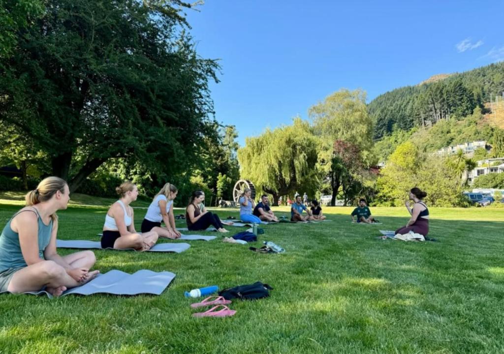 a group of people sitting on the grass in a park at The Flaming Kiwi Backpackers in Queenstown