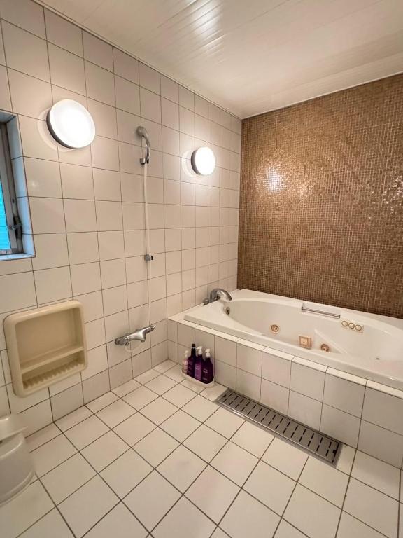 Saijō-chōにあるHotel JOYCEの白いタイル張りのバスルーム(バスタブ、シャワー付)