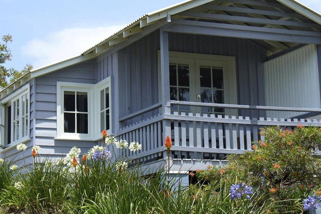 ein graues Haus mit einer weißen Veranda und Blumen in der Unterkunft Cottage 1 Hyams Beach Seaside Cottages in Hyams Beach