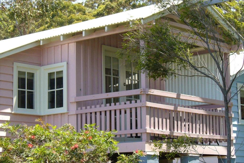 a pink house with a porch and a balcony at Cottage 2 Hyams Beach Seaside Cottages in Hyams Beach