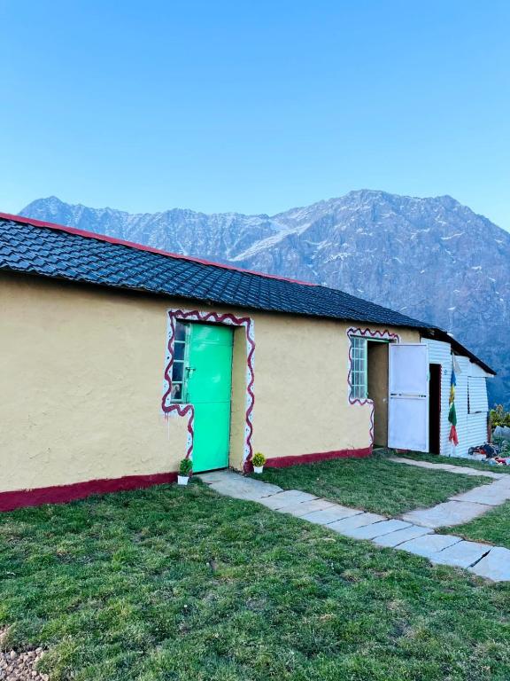 a building with a green door and mountains in the background at Thatharana Trek by Mountain Hikers - Mudhouse & Cafe in Dharmsāla