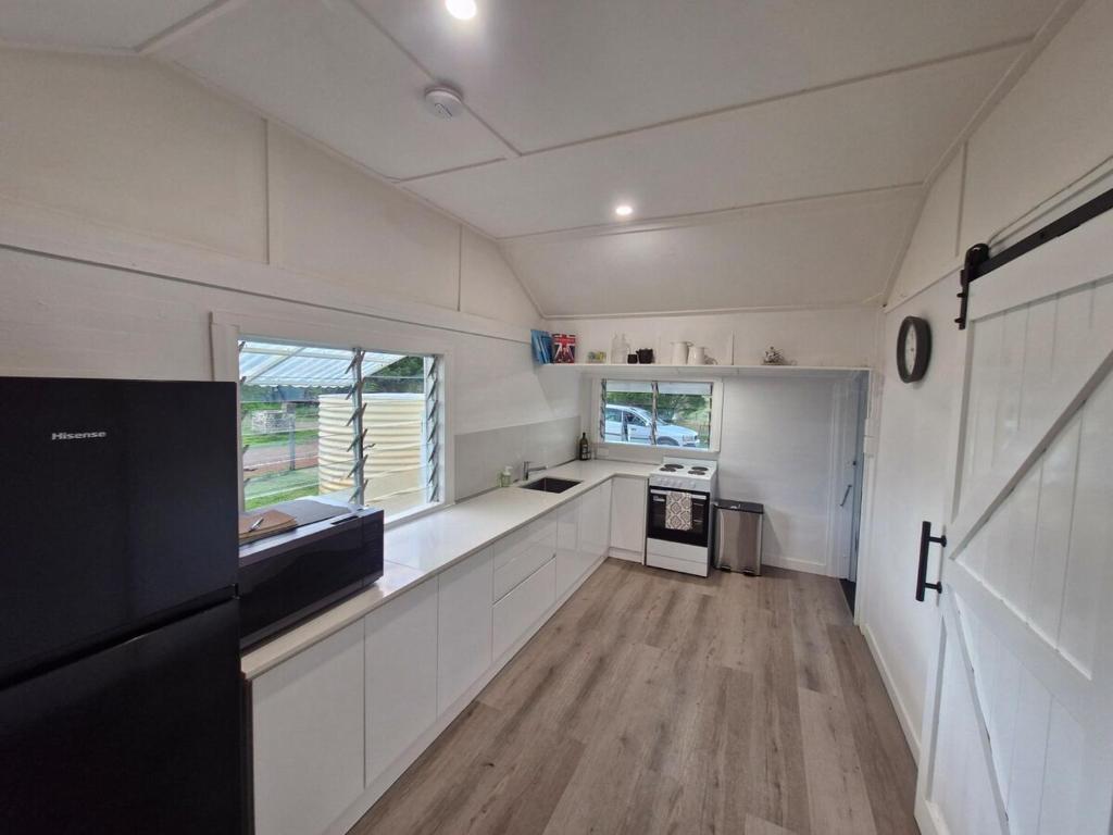 a kitchen with white walls and wood floors in a tiny house at Cottage on the Burnett, Mundubbera in Mundubbera