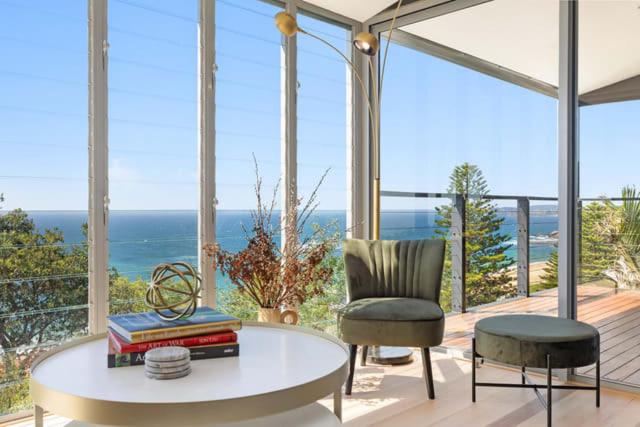 een woonkamer met een tafel en een stoel en de oceaan bij Sandcastle by Coast Hosting in Wamberal