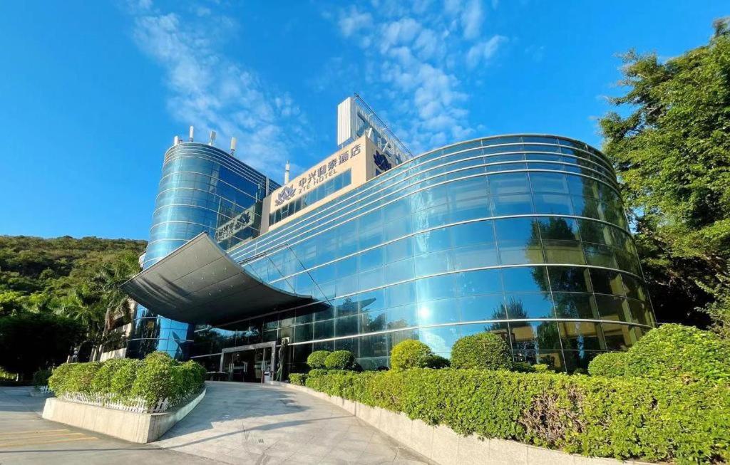 un gran edificio de cristal con árboles delante de él en ZTE Hotel Shenzhen, en Shenzhen