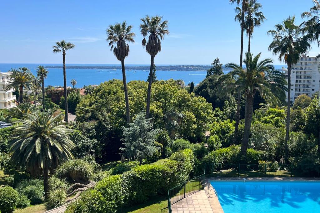 Elle offre une vue sur la piscine bordée de palmiers et l'océan. dans l'établissement Appartement Costebelle vue mer - Welkeys, à Cannes