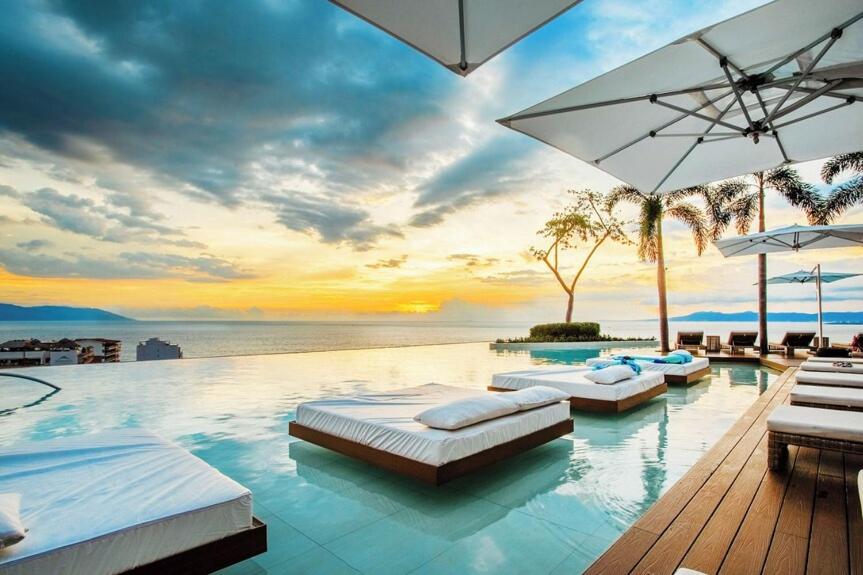 a swimming pool with four beds and an umbrella at BEST Views of PV-Banderas Bay from Rooftop Infinity Pool in Puerto Vallarta