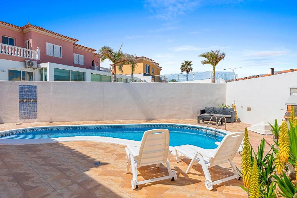 a swimming pool with two chairs and a house at Villa las dunas in El Médano