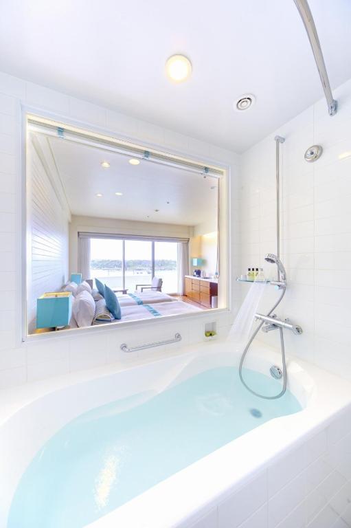 a bath tub in a bathroom with a large mirror at ANA InterContinental Manza Beach Resort by IHG in Onna