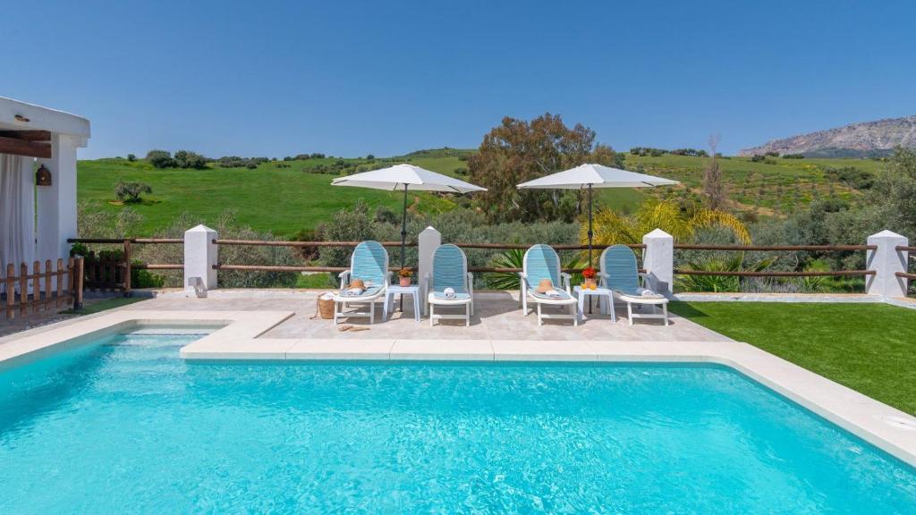 a swimming pool with blue chairs and umbrellas at Cortijo Casablanca Villanueva de la Concepción by Ruralidays in Villanueva de la Concepción