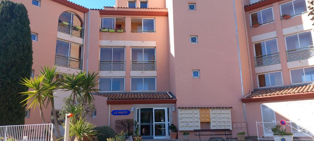 un bâtiment rose avec un palmier devant lui dans l'établissement Le Nautic YourHostHelper, à Saint-Raphaël