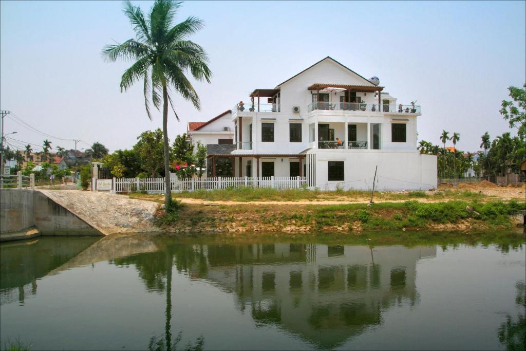 una casa con una palmera junto a un cuerpo de agua en Azalea Homestay, en Hoi An