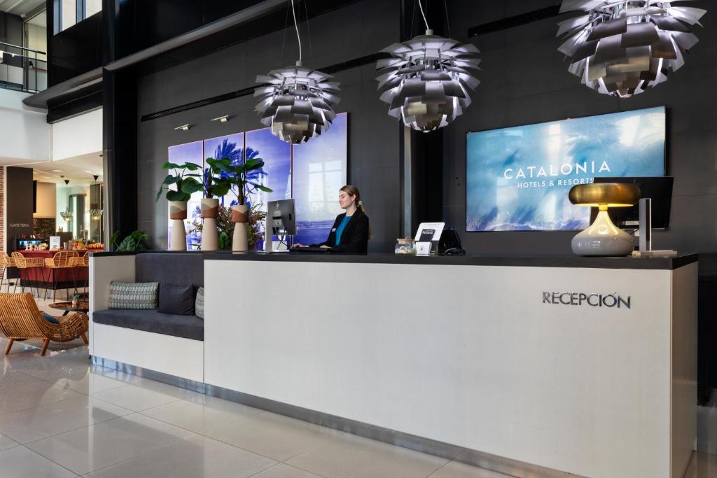 a woman standing at a reception desk in a lobby at Catalonia Málaga in Málaga