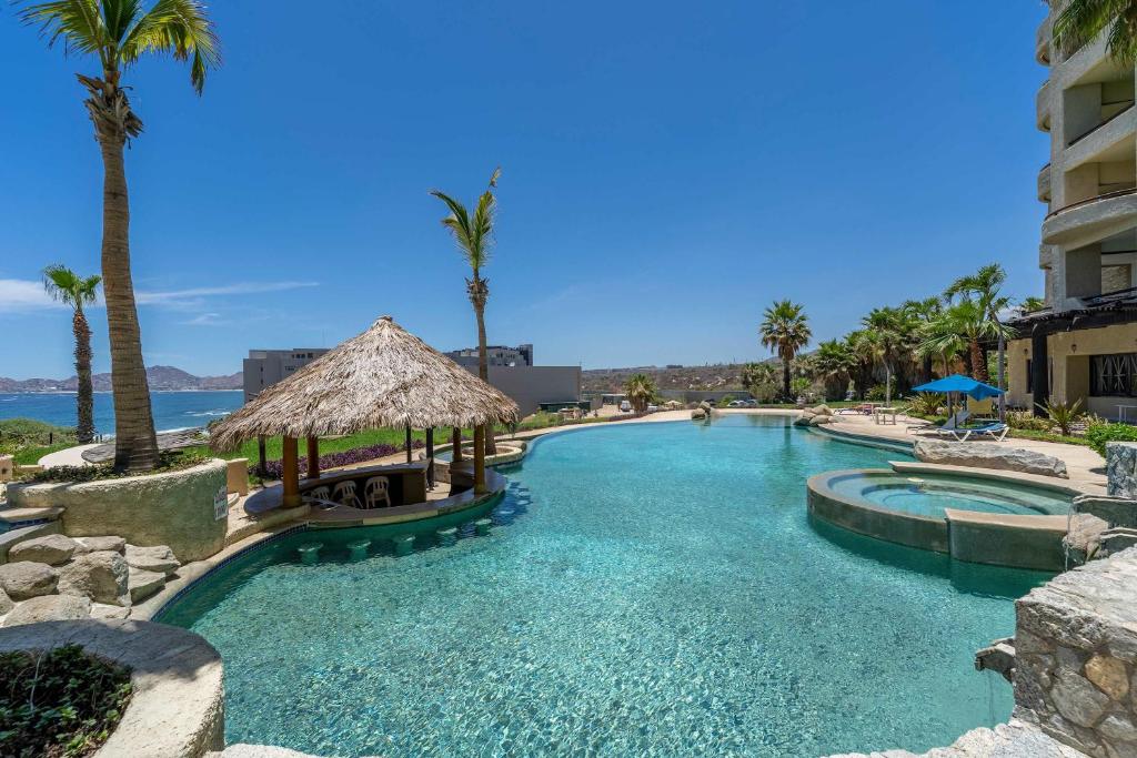 a large swimming pool with palm trees and a building at Stunning 2 BR with Ocean Views & Jacuzzi by the Beach in Cabo San Lucas