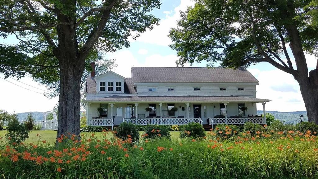 a white house with a porch and trees and flowers at Hoppy Hill Farm House in Dover Plains