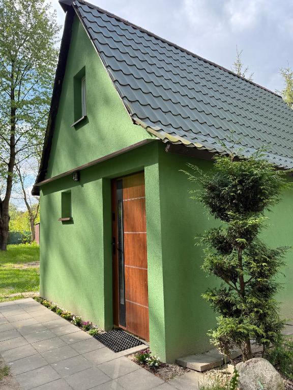 a green house with a black roof and a door at Domek w lesie in Gnojno
