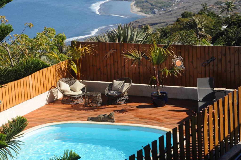 a swimming pool on a wooden deck with chairs and the ocean at Leu Bleu Austral in Saint-Leu