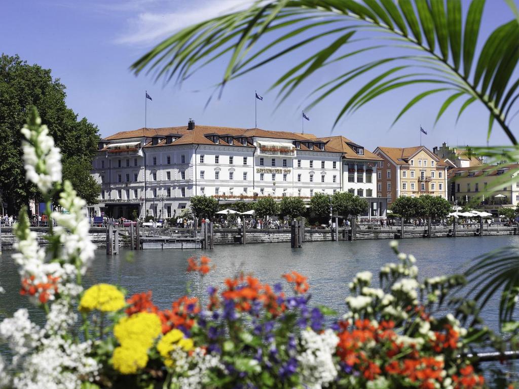 a large white building next to a river with flowers at Hotel Bayerischer Hof in Lindau