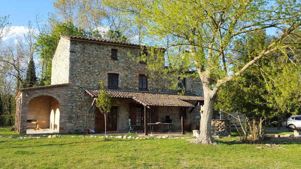 une maison en pierre avec un arbre en face de celle-ci dans l'établissement Can More El Pasteral, à La Cellera de Ter