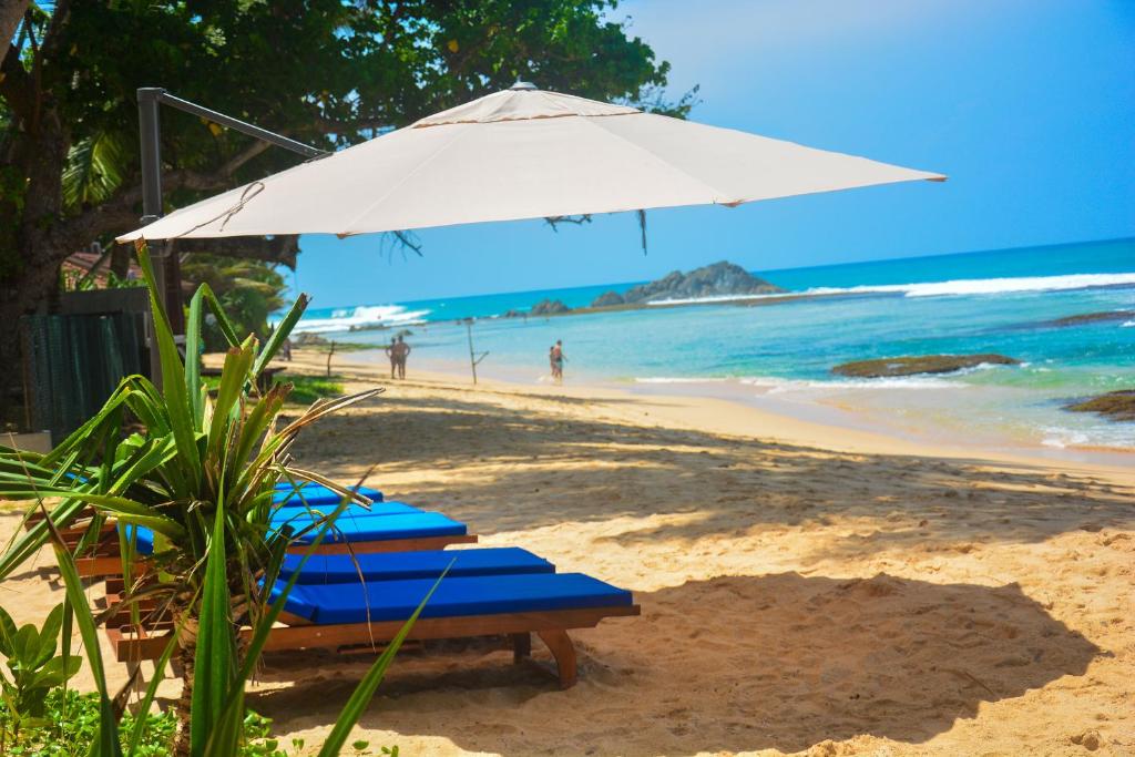 two lounge chairs and an umbrella on a beach at Sayura Beach Hotel in Unawatuna