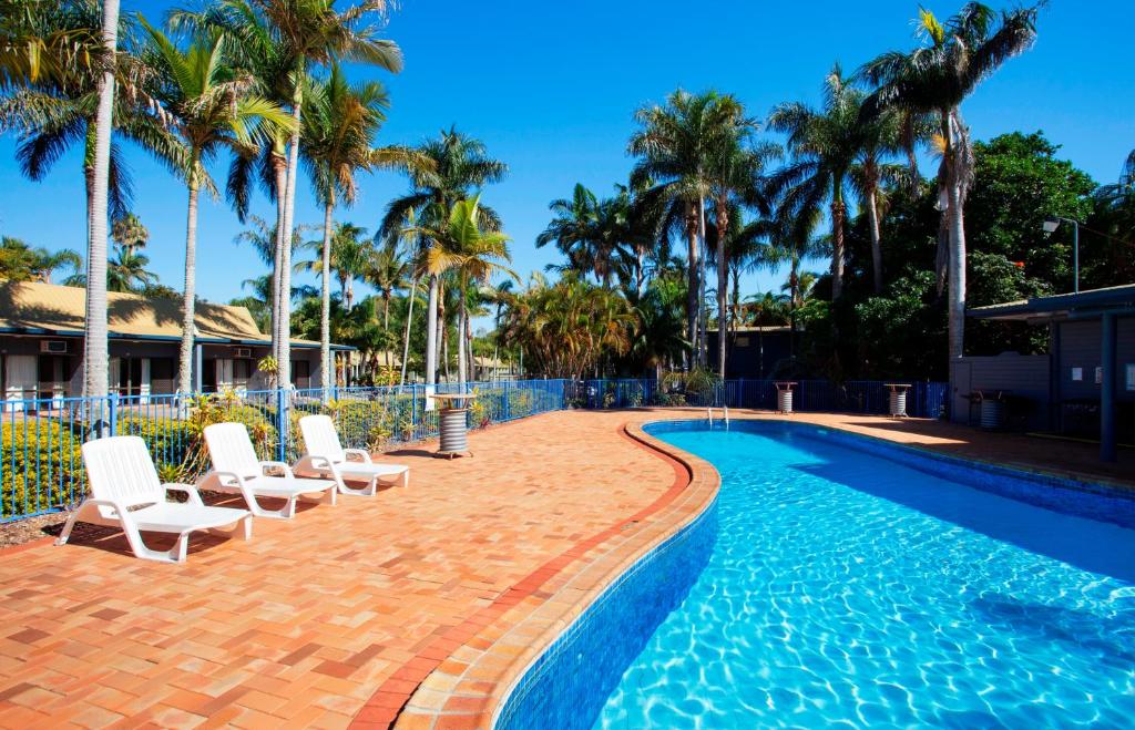 a swimming pool with white chairs and palm trees at Kondari Hotel in Hervey Bay