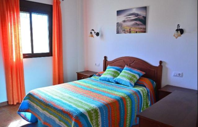 a bedroom with a bed with a colorful blanket and a window at Residencial La Teja in Zahora