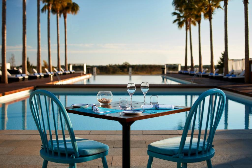 a table with two chairs and wine glasses next to a pool at Victoria Golf Resort and Spa Managed by Accor in Vilamoura
