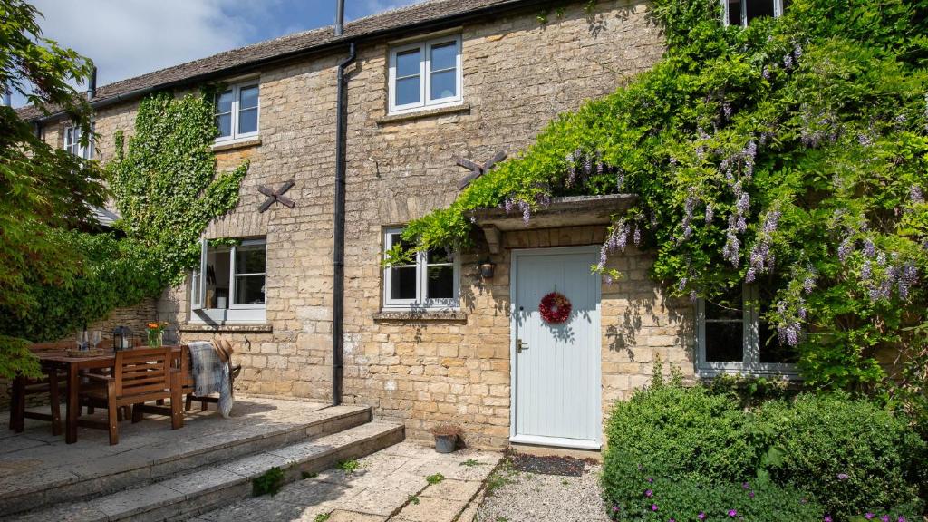 a brick house with a white door and a table at Honeywick Cottage in Stow on the Wold