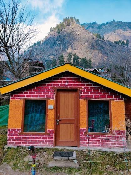 Una pequeña casa de ladrillo con una puerta frente a una montaña. en Parvati Hill Cottage By Soma Stays, en Kasol