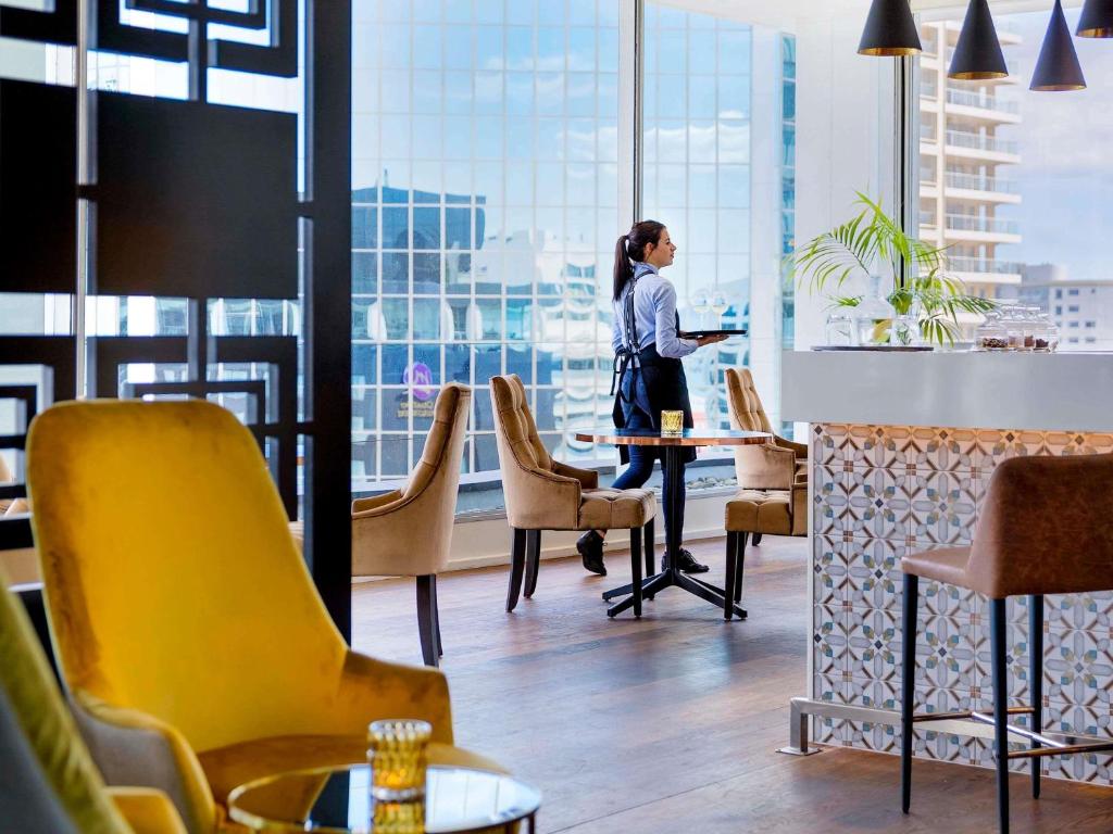 a woman standing at a table in a room with a window at Mövenpick Hotel Auckland in Auckland