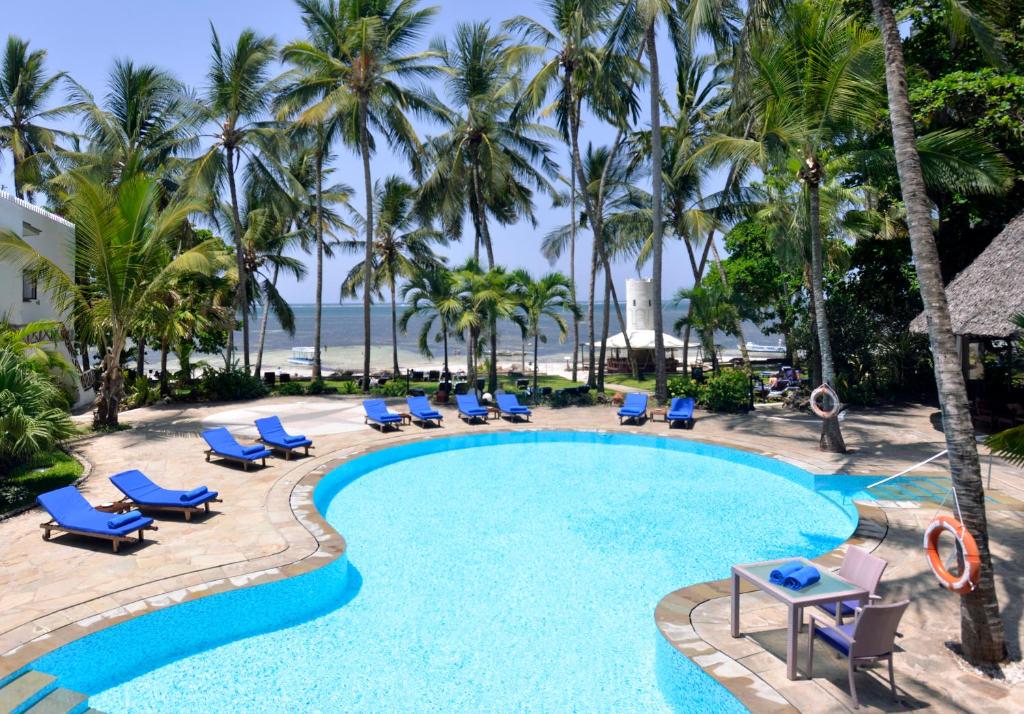 a pool with chairs and palm trees and the ocean at Severin Sea Lodge in Mombasa