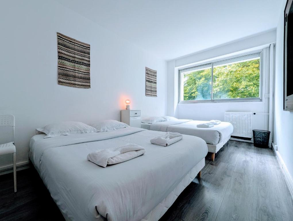 two beds in a white room with a window at Comfortable appart near Paris in Colombes