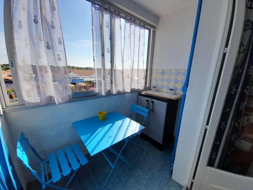 - une petite table bleue et des chaises dans une chambre avec fenêtre dans l'établissement Charmant T2 à 1min de la plage avec parking privé et commodités à proximité ! - FR-1-324A-69, à Saint-Hilaire-de-Riez