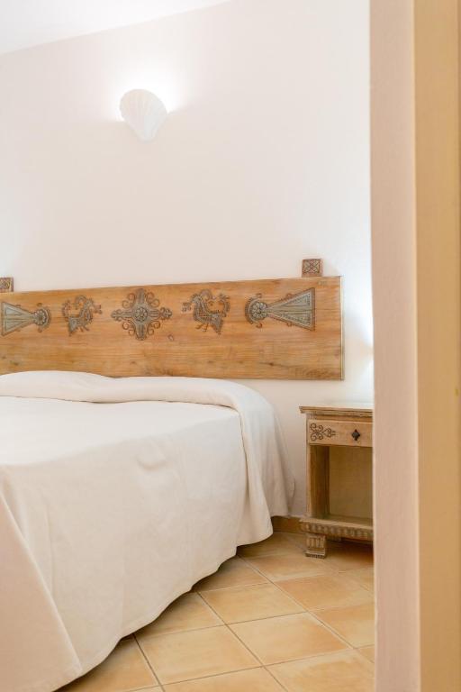 a bedroom with a white bed with a wooden headboard at Porto Giunco Residence in Villasimius