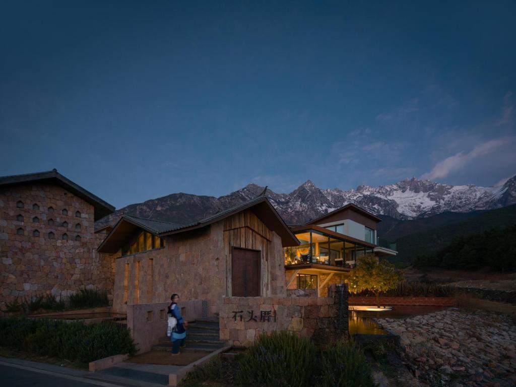 Una mujer parada frente a una casa con montañas. en Lijiang Snow Mountain stone house, en Lijiang