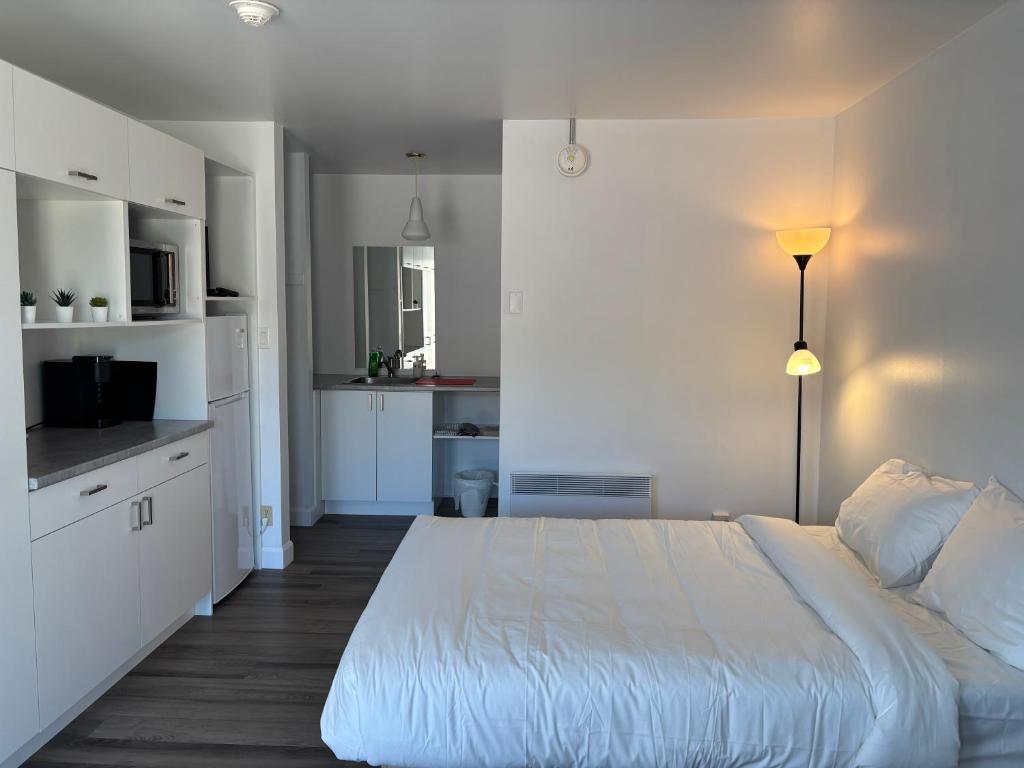 a white bedroom with a large bed and a kitchen at Hébergements ASLC Baie-Comeau in Baie-Comeau