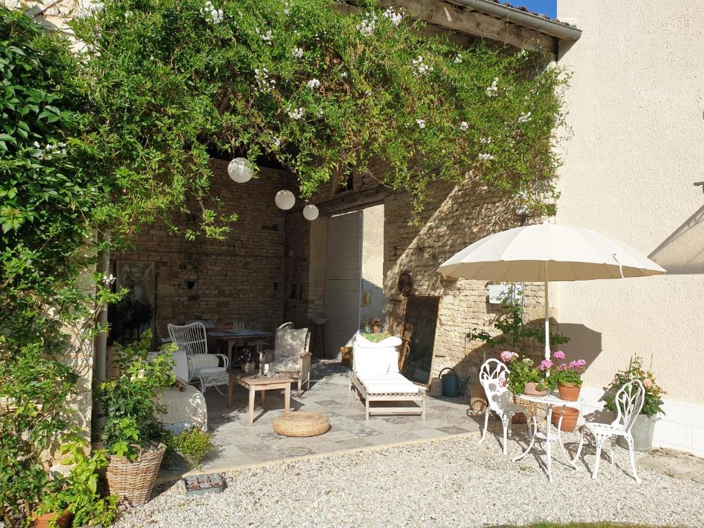 un patio avec une table, des chaises et un parasol dans l'établissement La Maison Ânanda, à Aigre