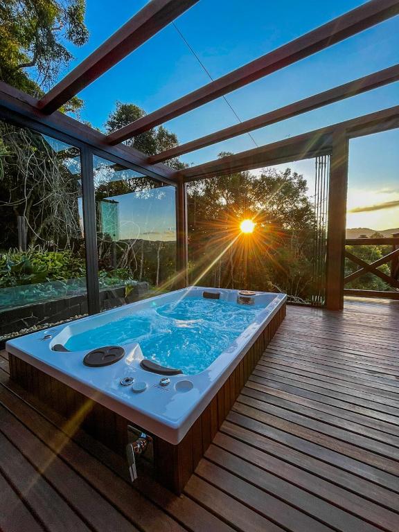 a hot tub on a deck with the sun setting at Rancho Texel Chalé de Luxo in Rancho Queimado