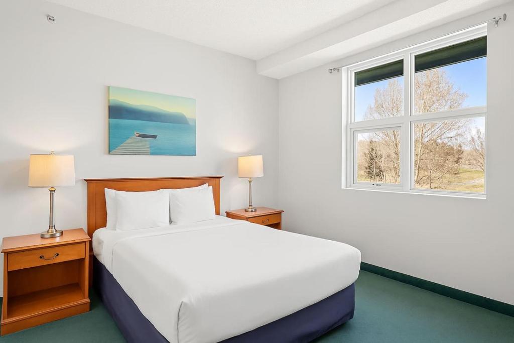 a white bedroom with a bed and two windows at Serene 1BR Retreat Mtn Views, Pool, and Hot Tub in Canmore