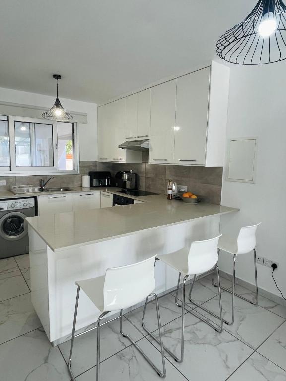 a kitchen with white cabinets and a counter with white chairs at Sea Breeze - Oroklini in Voroklini