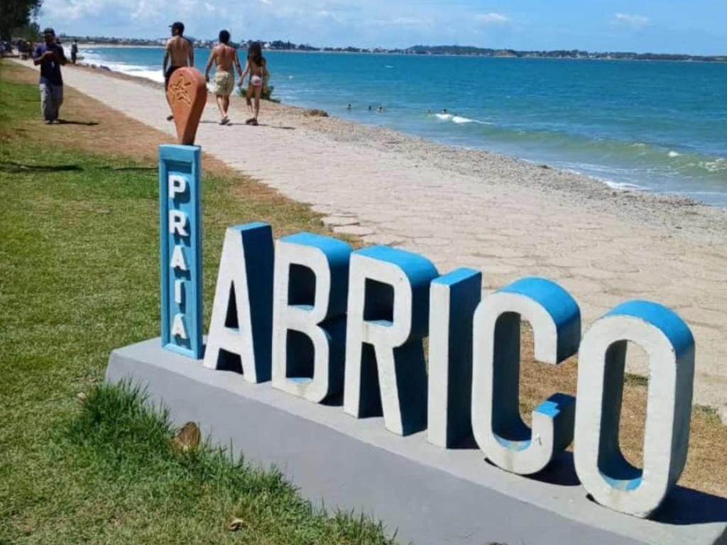 a sign at a beach with people walking on the beach at Verde Mar Abricó 2 in Rio das Ostras