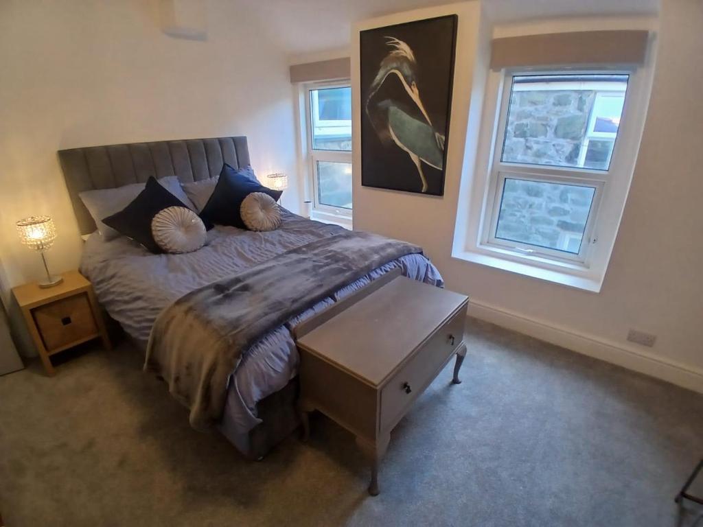 a bedroom with a bed with a table and two windows at Seasalt Apartment in Barmouth