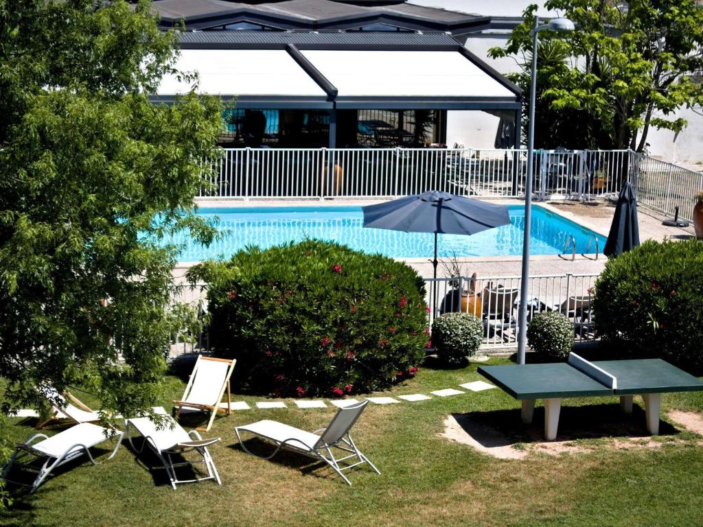 una piscina con sillas, una mesa y una sombrilla en ibis Styles Avignon Sud, en Aviñón